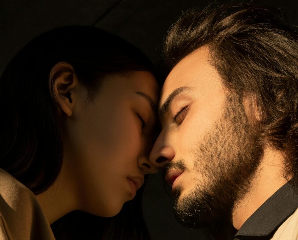 Side view of a couple sharing an intimate moment with closed eyes under soft lighting.